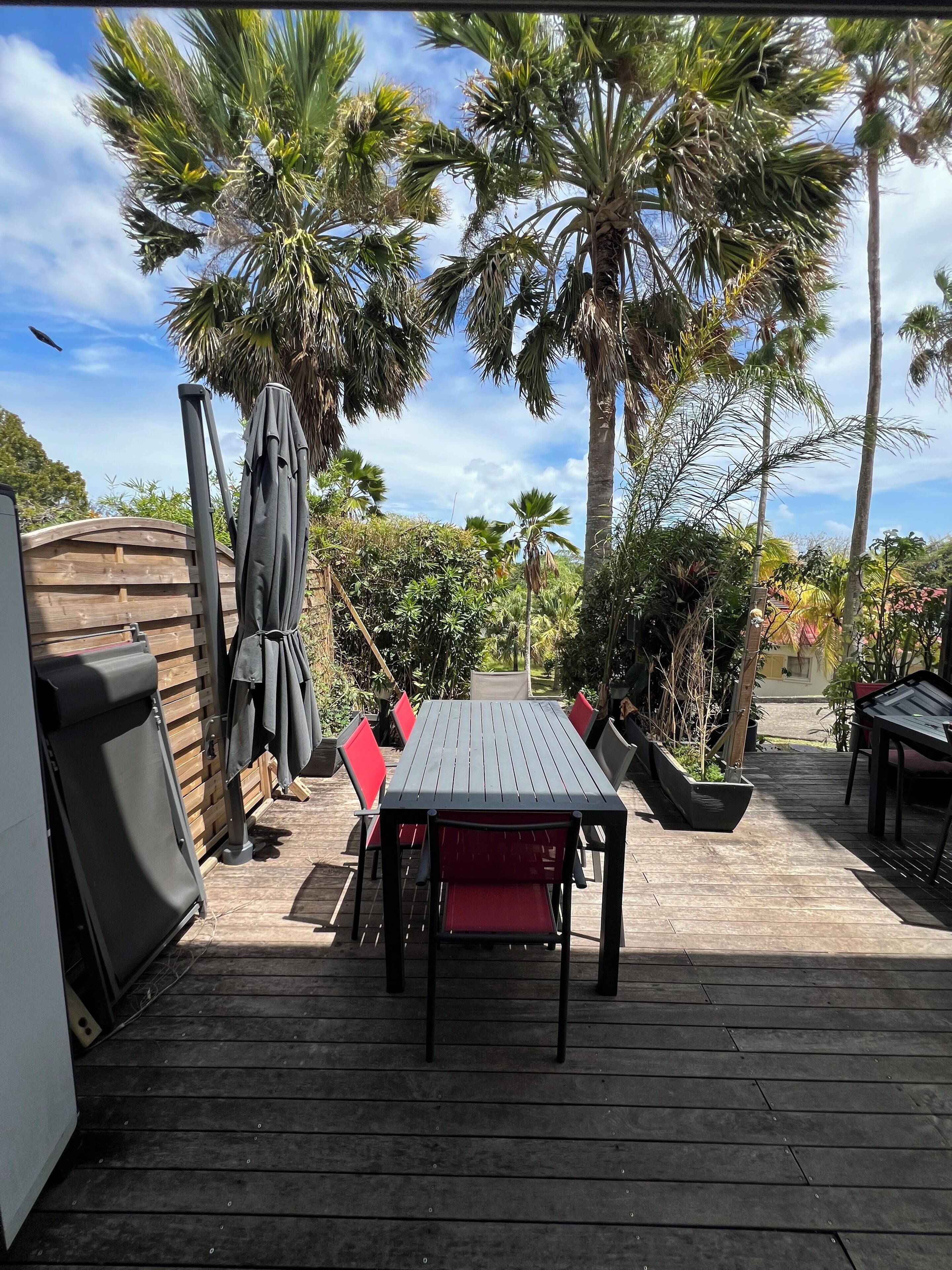 Une terrasse en bois avec une table et des chaises, entourée de palmiers et d’une clôture en bois.