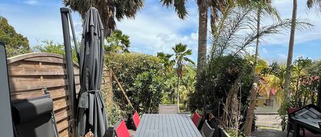Une terrasse en bois avec une table et des chaises, entourée de palmiers et d’une clôture en bois.