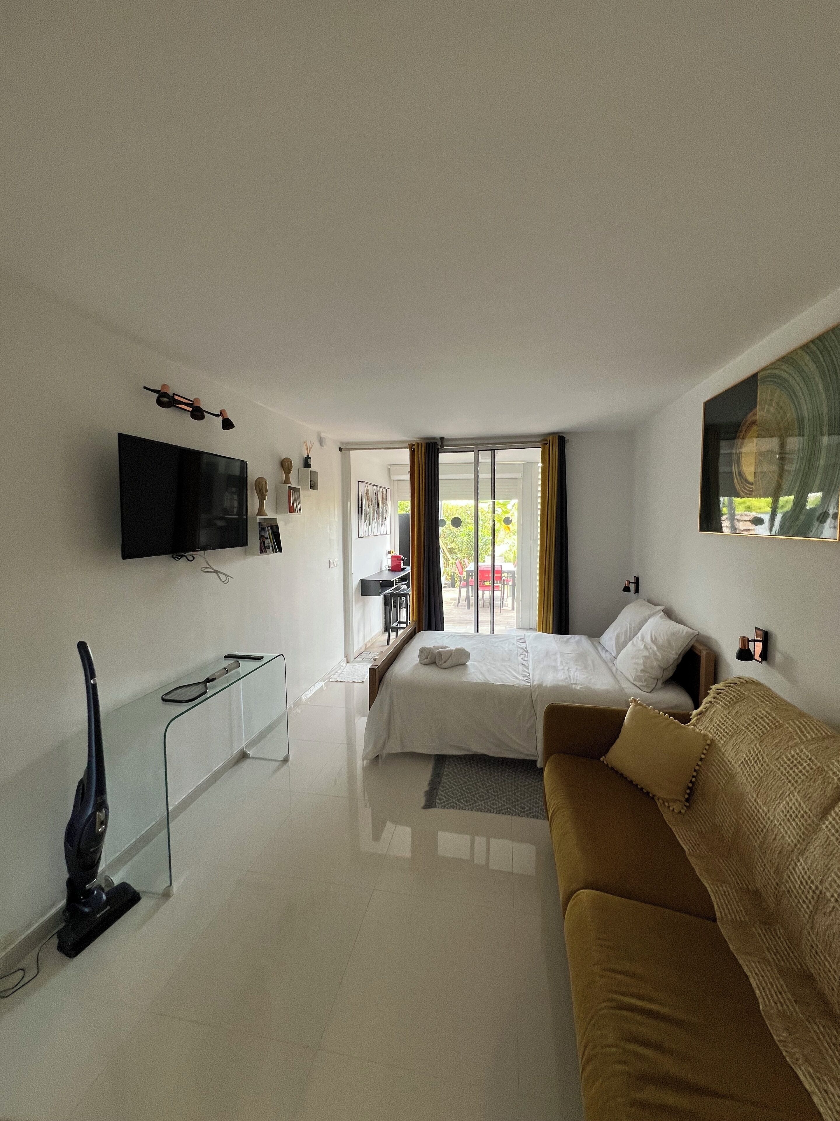 Une chambre d’hôtel moderne, dotée d’un grand lit, d’un canapé, d’une télévision et d’une porte-fenêtre coulissante donnant sur l’extérieur.