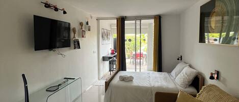 Una moderna camera d'albergo con un ampio letto, un divano, una TV e una porta scorrevole in vetro che dà sull'esterno.