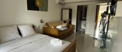 A hotel room with a large bed, a sofa, a dining area, and a kitchen.