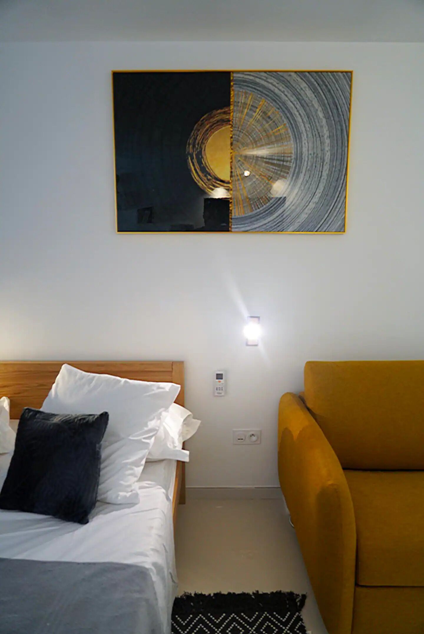 A hotel room with a bed, a yellow armchair, and a wall-mounted artwork.