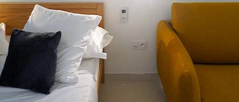 A hotel room with a bed, a yellow armchair, and a wall-mounted artwork.