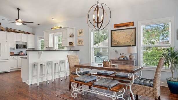 A modern kitchen with white cabinetry, a wooden dining table with bar stools, and a chandelier. - Good Tides Getaway! (Beaufort)