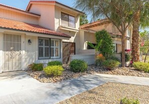 A two-story house with a tiled roof, a gated entrance, and a landscaped garden with various plants and a palm tree. - Modern Palm Springs Escape! (Palm Springs)