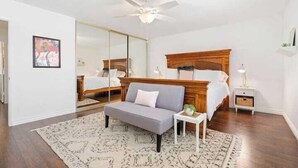 Ein Schlafzimmer mit Bett, einer Couch, einem kleinen Tisch, einem Nachttisch, einem Deckenventilator und einem Spiegel.