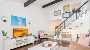 Ein modernes Wohnzimmer mit Flachbildfernseher, einer weißen Unterhaltungsanlage, einer Couch, einem Couchtisch und einer Treppe mit Geländer.