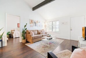 A living room with a brown sofa, a coffee table, and a rug. There is a plant, a lamp, and a door in the background. - Modern Palm Springs Escape! (Palm Springs)