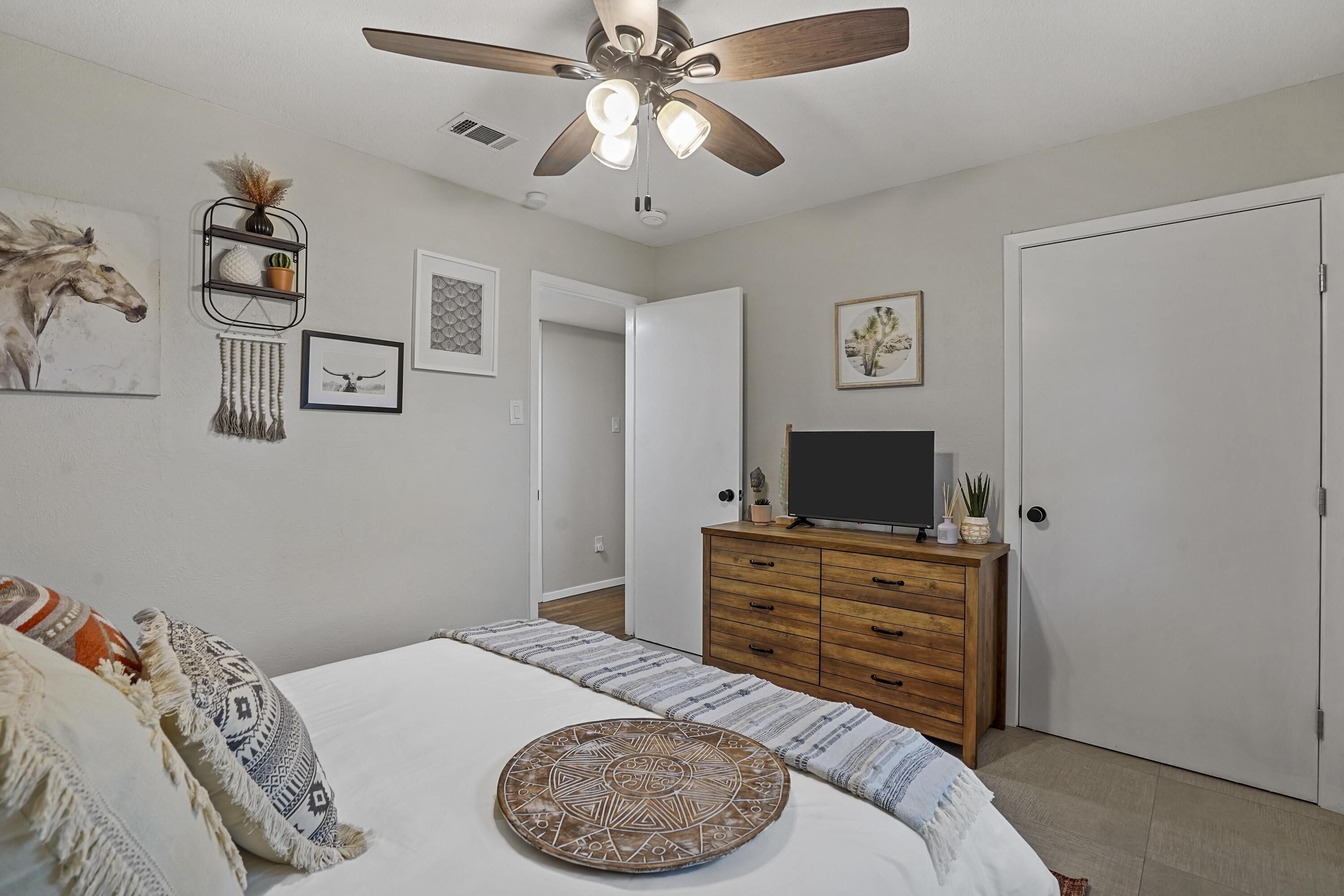 A bedroom with a bed, a wooden dresser, a ceiling fan, and a television.