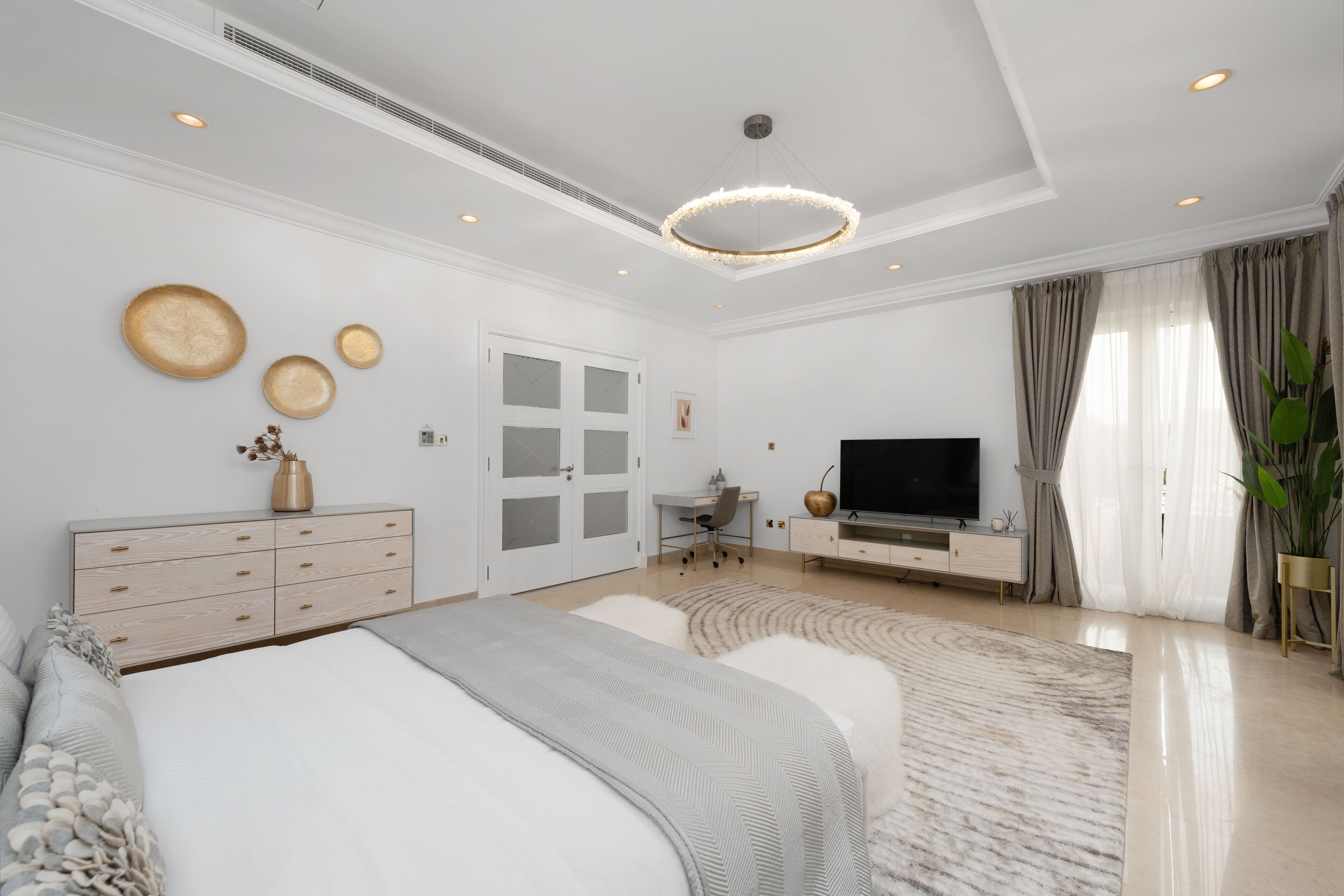 A modern bedroom with a large bed, a desk, a TV, and a decorative wall.