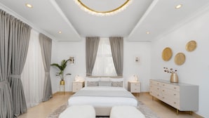A modern bedroom with a large bed, bedside tables, a dresser, and a chandelier.