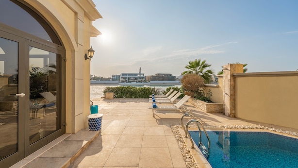 A pool area with a clear view of the sea, a modern building in the background, and a well-maintained patio with lounge chairs.