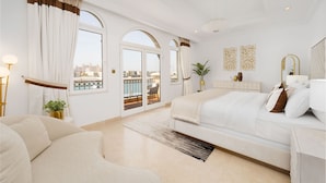 A spacious bedroom with a large bed, a sofa, and a view of a cityscape through the balcony doors.