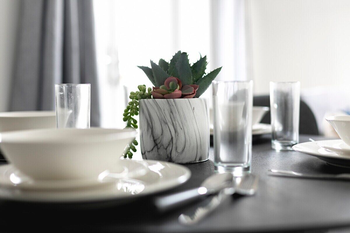 A dining table with a white bowl, clear glasses, and a marble vase with a succulent plant.
