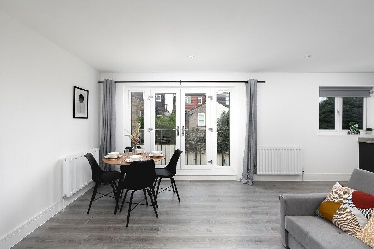 Ein modernes Wohnzimmer mit Essbereich, großen Schiebeglasfenstern zum Balkon und einem grauen Sofa.