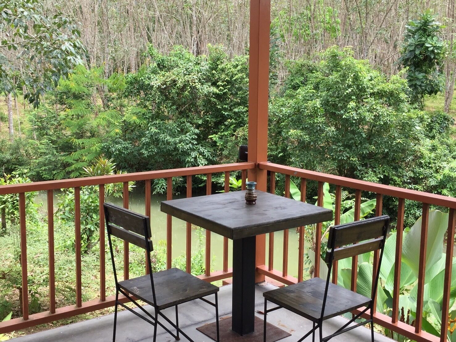 Ein Balkon mit Tisch und zwei Stühlen, umgeben von einem Geländer, mit Blick auf eine üppige grüne Landschaft.