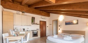 Ein modernes Hotelzimmer mit Holzboden, einer Küchenzeile, einem Essbereich und einem Bett mit ordentlich gefalteten Handtüchern.