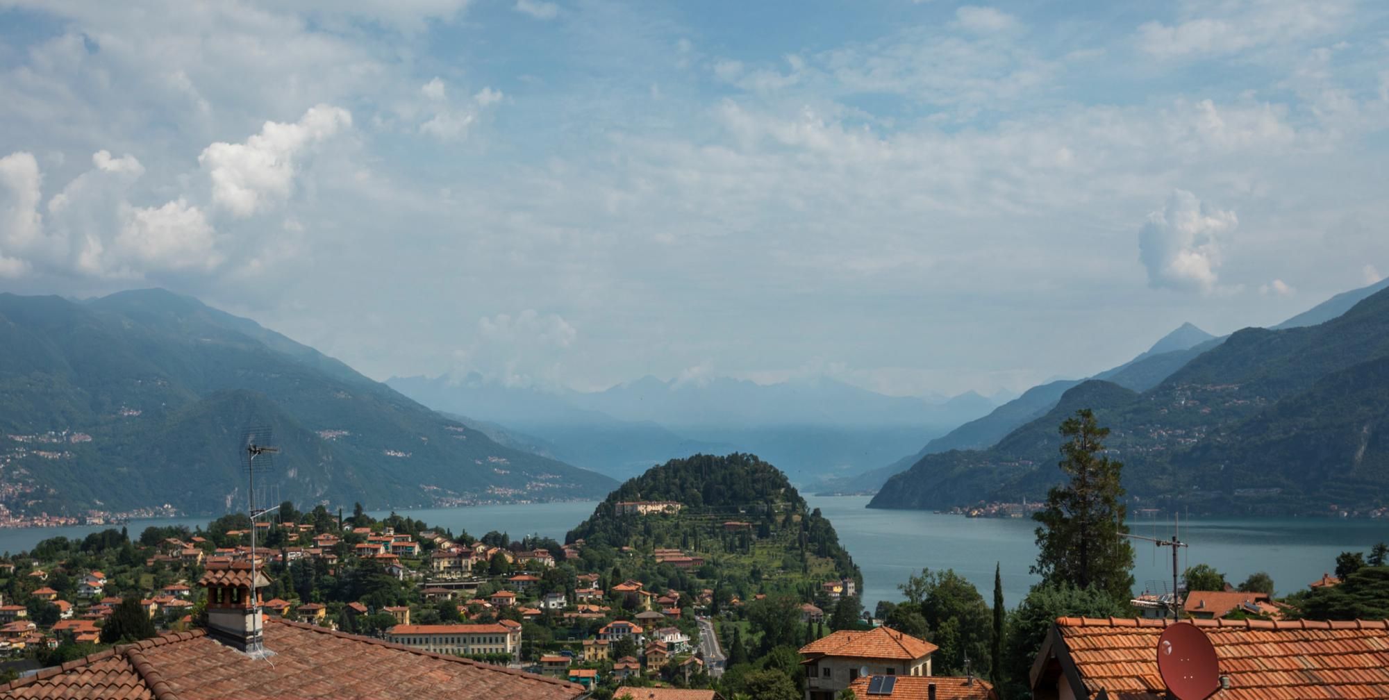 Eine Küstenstadt mit terrakottafarbenen Dächern, einem See und Bergen im Hintergrund.