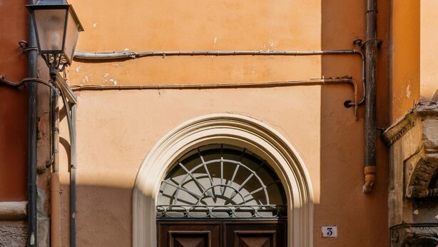 A dark wooden door with a decorative arch above it, set in a building with a beige wall. There are two bollards in front of the door. - Appartamento al Ghetto Ebraico by Wonderful Italy (Bologna)