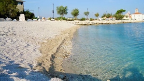 A beach with clear water, a rocky shoreline, and buildings in the background. - Apartments Ivan (Solin)