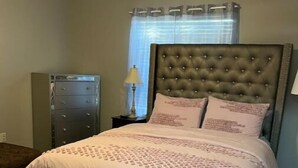 Una camera da letto con un letto, un comodino, una cassettiera e una finestra con tende.