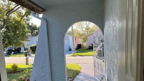 Un portico coperto con prato sintetico, una panchina e vista su una strada residenziale.