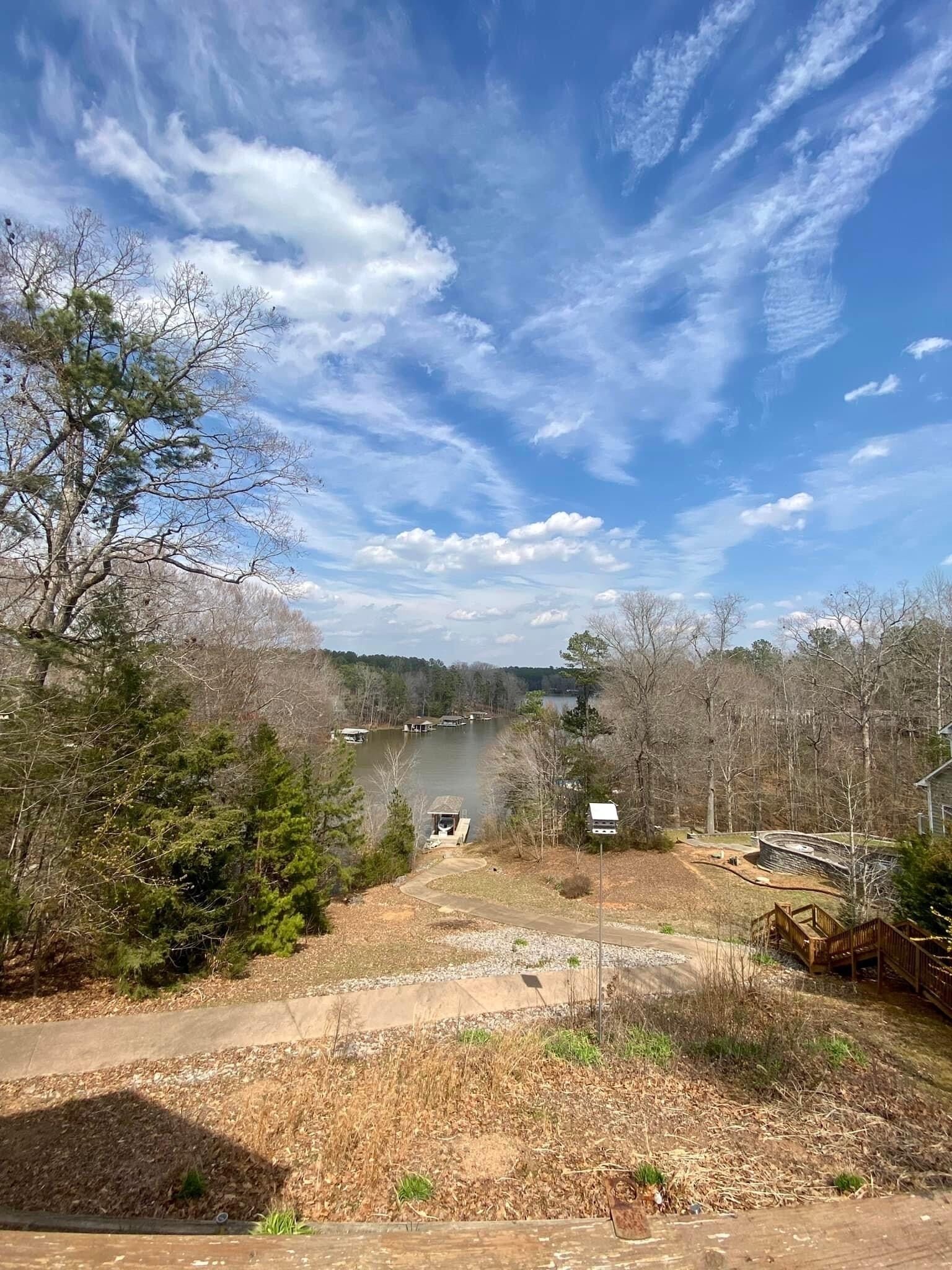 A lakeside property with a dirt path leading to a dock, surrounded by trees and a clear sky.