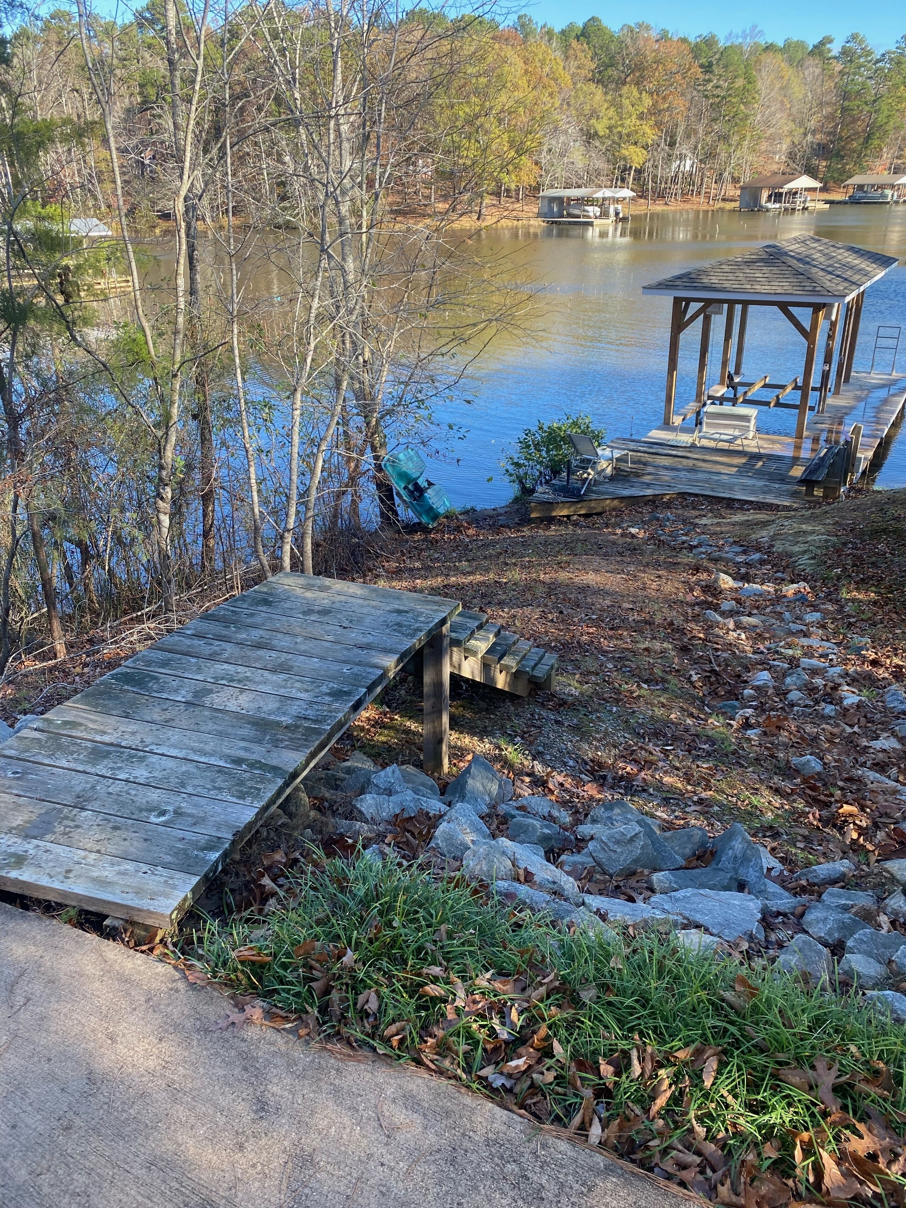 A wooden dock extending into a lake, surrounded by trees and a small wooden structure with benches.