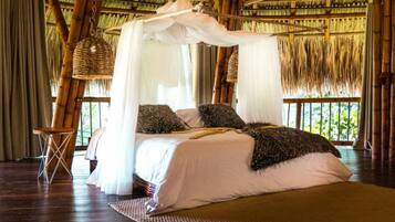 A room with a thatched roof, a bed with white bedding, and a woven chair.