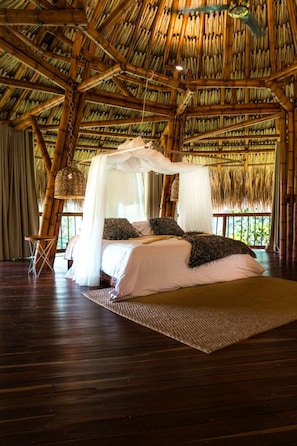 A room with a thatched roof, a bed with white bedding, and a woven chair.