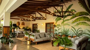 A spacious living area with a high ceiling, wooden beams, and a large chandelier. There are multiple sofas and a variety of potted plants. - El Río Hotel (Sonson)