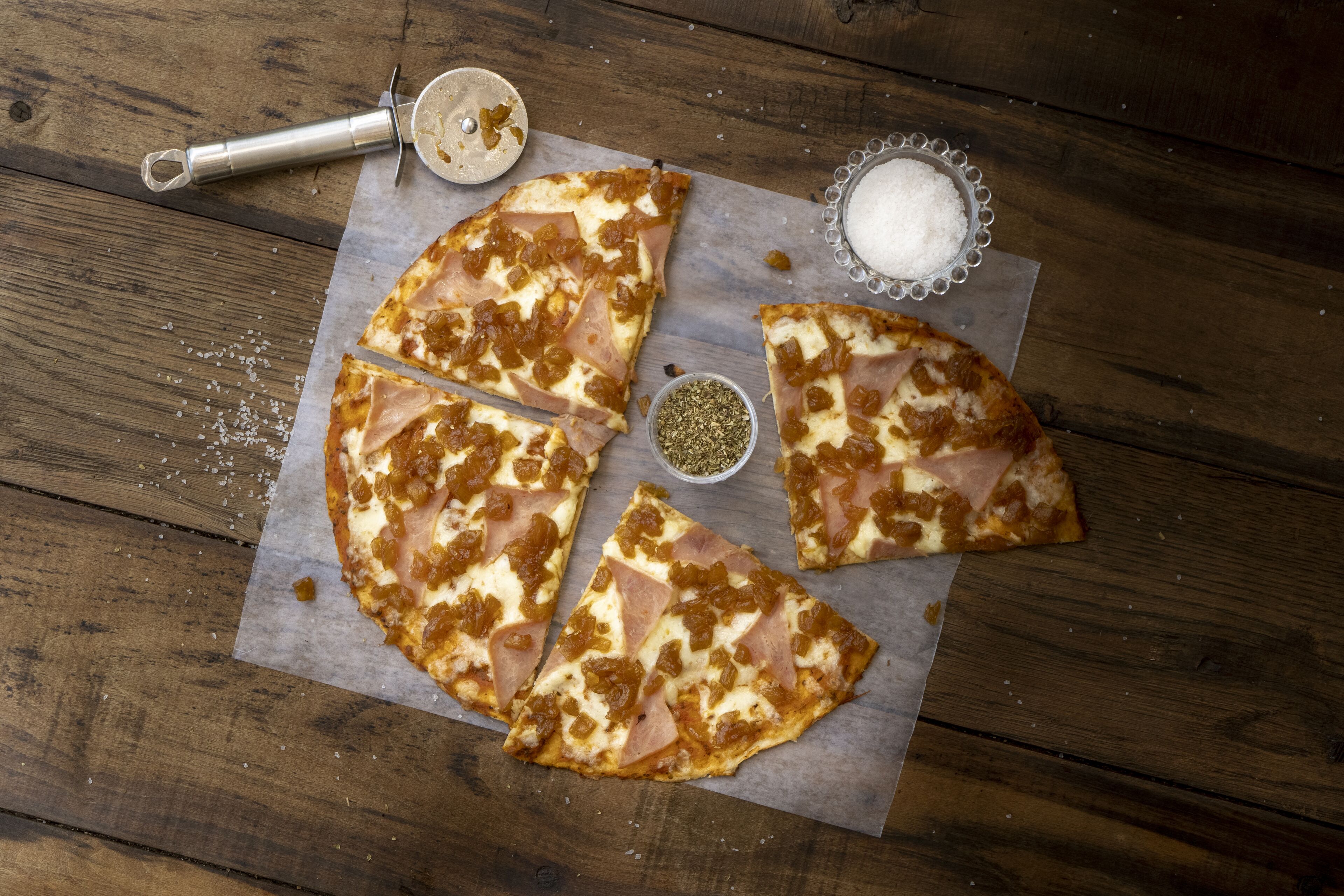 Una pizza amb formatge i pernil sobre una taula de fusta.