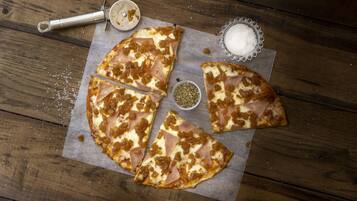 Una pizza amb formatge i pernil sobre una taula de fusta.