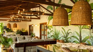 A spacious room with a long dining table, hanging wicker lamps, and a mural of tropical plants. - El Río Hotel (Sonson)
