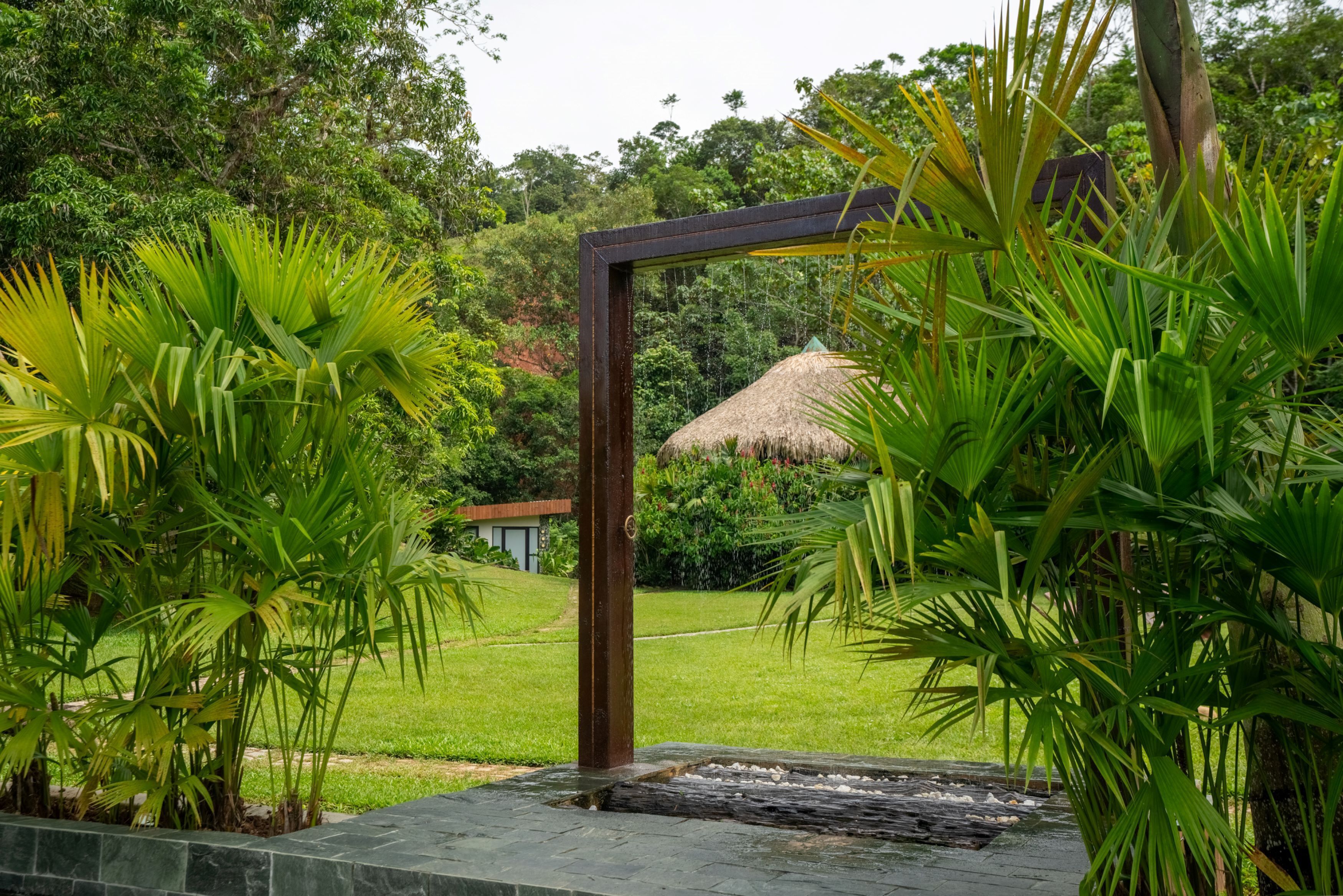 Un jardín tropical con una estructura de techo de paja, rodeado de exuberante vegetación y un sendero de piedra.