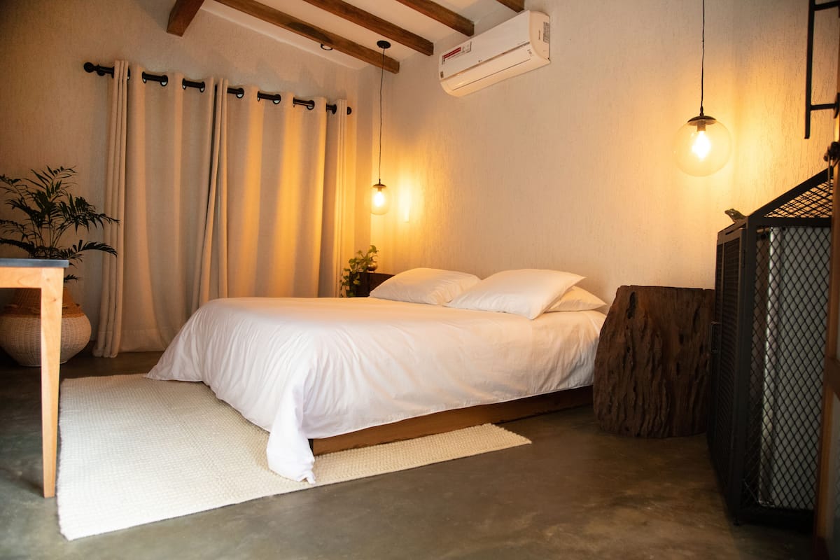 A bedroom with a bed, a desk, a plant, and a wooden bench.