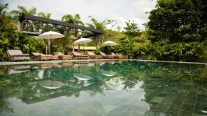 A clear pool with lounge chairs and umbrellas, surrounded by lush greenery. - El Río Hotel (Sonson)