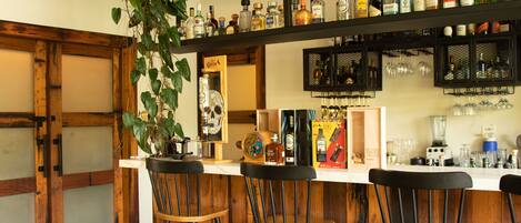 Zona de bar con vigas de madera, taburetes y una variedad de botellas y vasos en estantes.