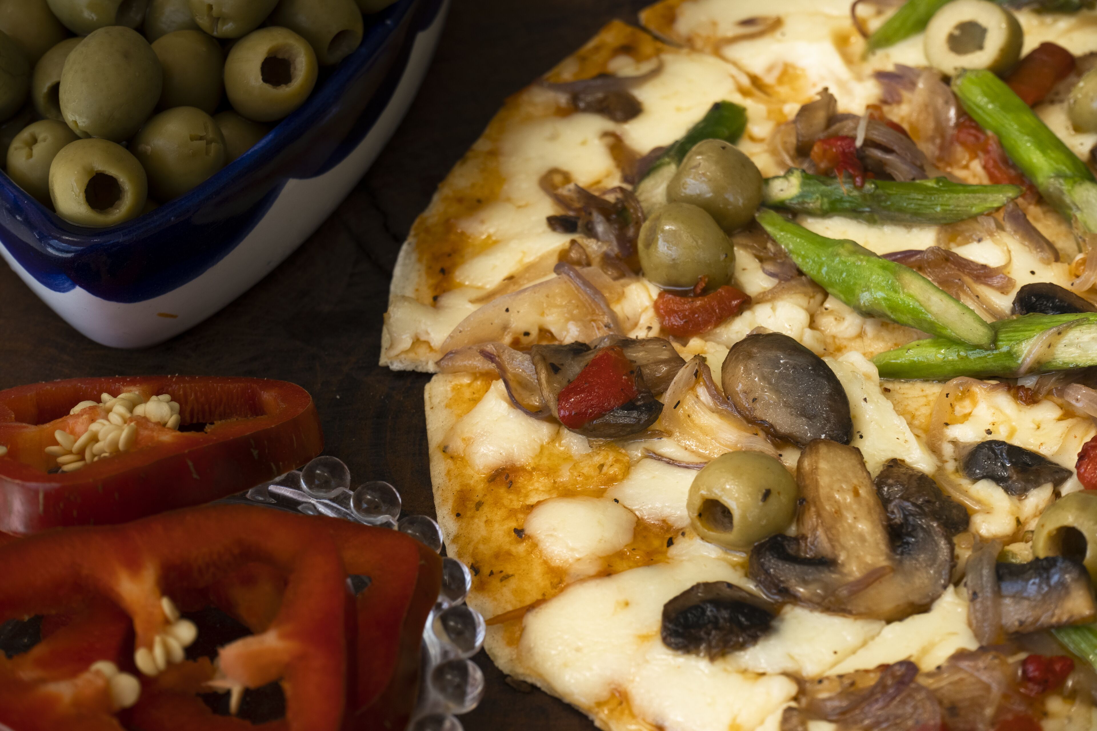 Una pizza con diferentes ingredientes y un cuenco de aceitunas.