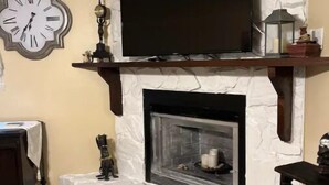 Ein Wohnzimmer mit Kamin aus Stein, einer Wanduhr und einem Flachbildfernseher.