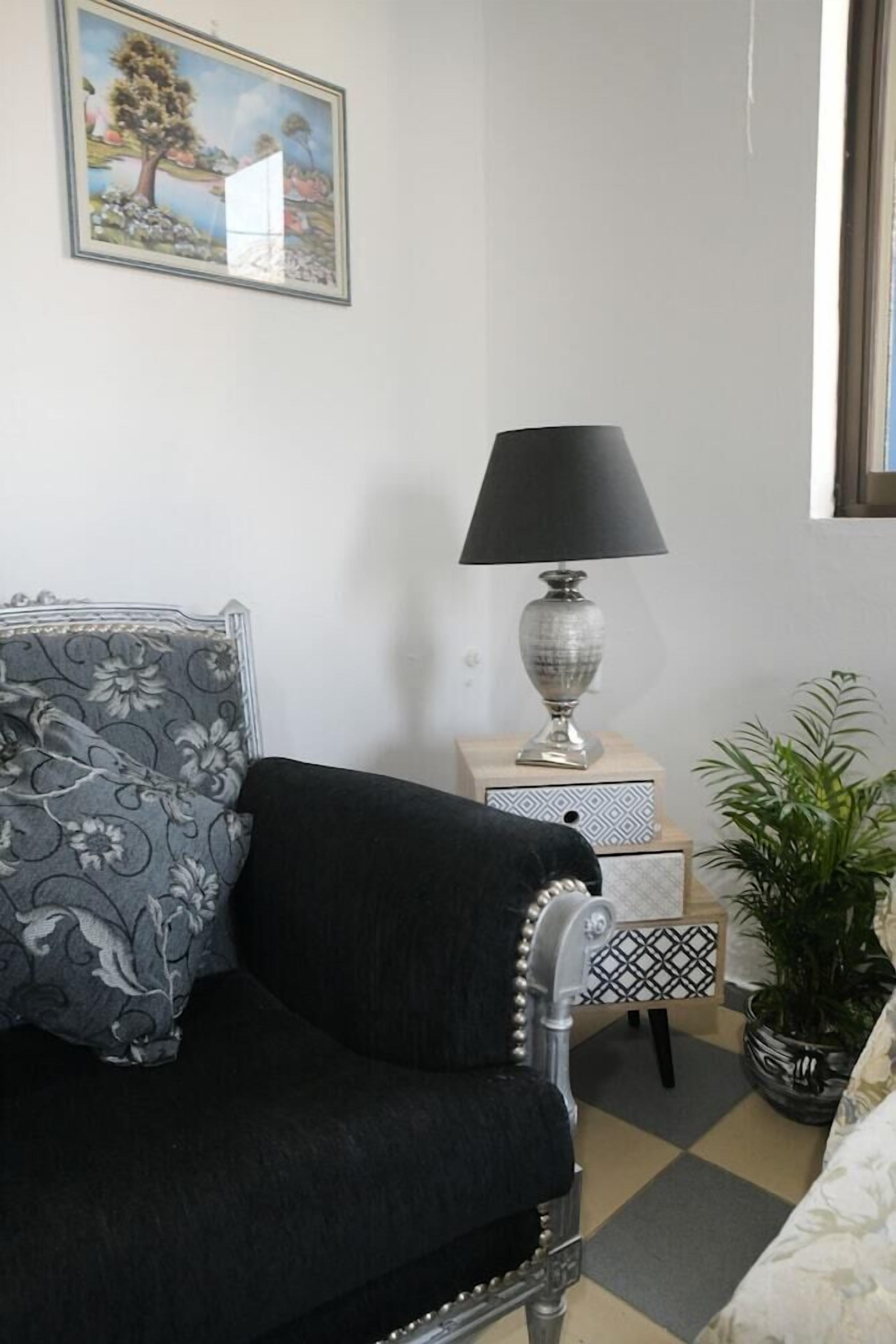 Une pièce comprenant un canapé, une lampe, une table d’appoint, une plante en pot et un tableau accroché au mur.