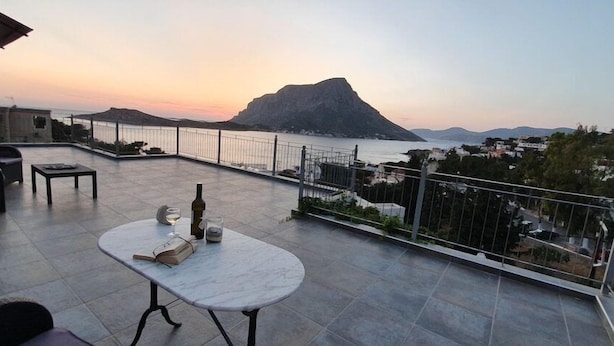 Terraço com mesa, cadeiras e vista para o mar e uma montanha.