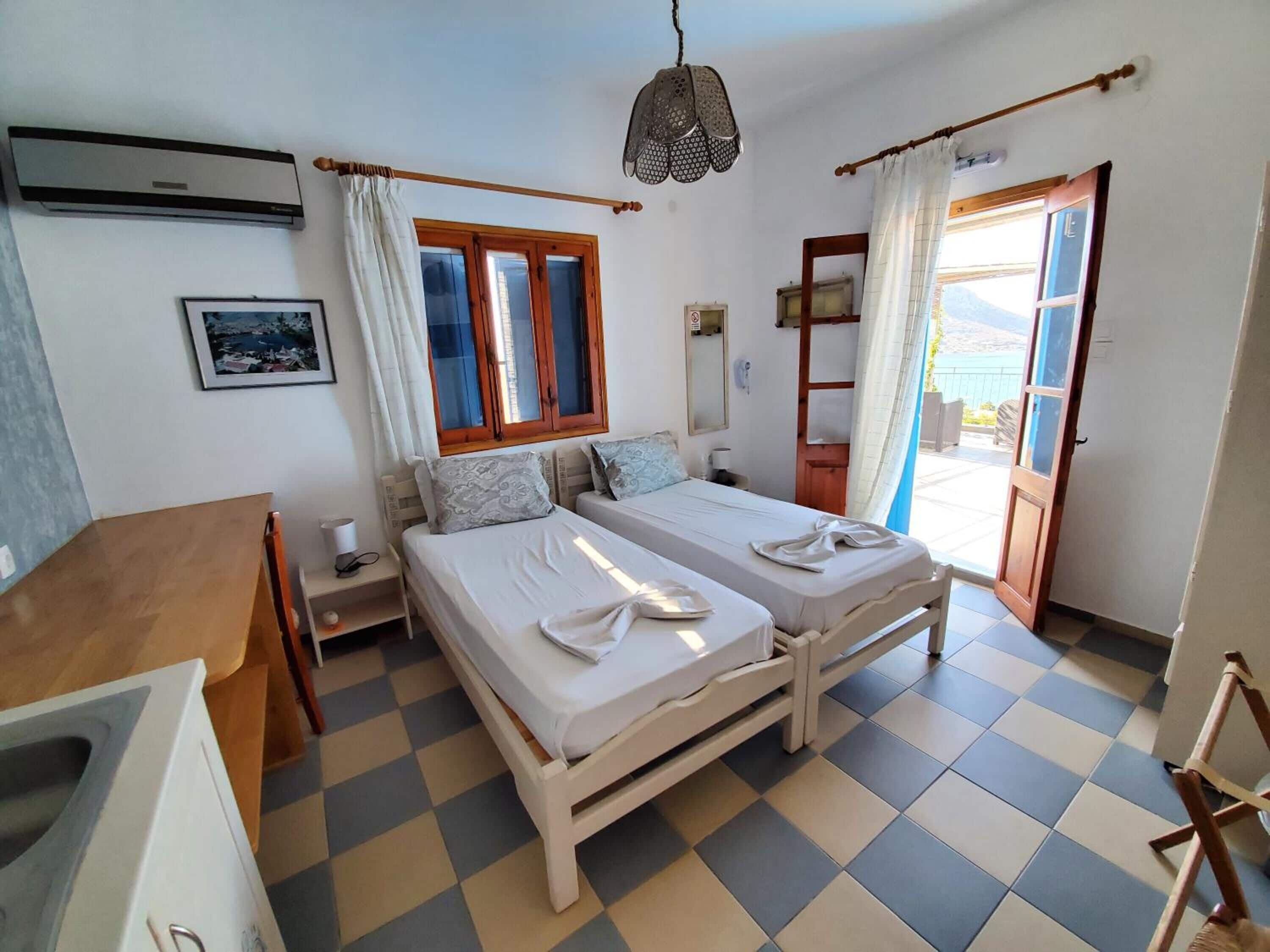 A room with two beds, a desk, a chair, a hanging light fixture, and a window with curtains.