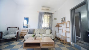 Um quarto com sofá, mesa de centro de madeira, cadeira, guarda-roupa e janela com cortinas.