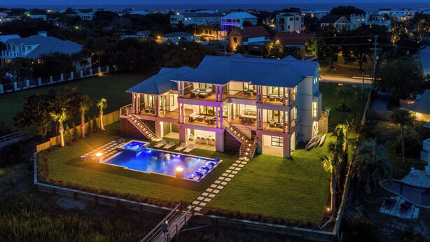 A multi-story house with a swimming pool, surrounded by a well-maintained lawn and palm trees. - Waterfront Home with Deep Water Dock (Isle of Palms)