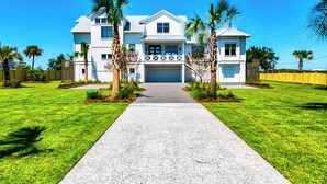 A two-story house with a front driveway, palm trees, and a well-maintained lawn. - Waterfront Home with Deep Water Dock (Isle of Palms)