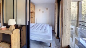 A bedroom with a bed, a wooden desk, a lamp, and a view of the outdoors.