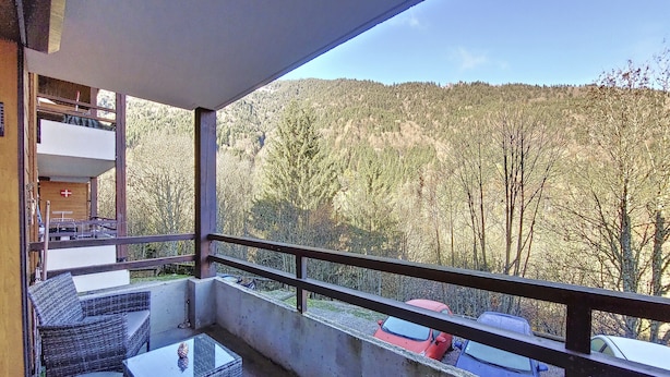 A balcony with wicker furniture, a concrete floor, and a view of a forested hillside.
