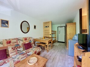 Un salon chaleureux avec un canapé à motifs, une table à manger en bois et un téléviseur posé sur un meuble en bois.