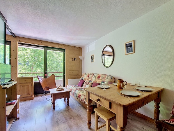 Une pièce chaleureuse avec une table en bois, un canapé agrémenté de coussins à motifs, un miroir au mur et une fenêtre donnant sur un paysage verdoyant.